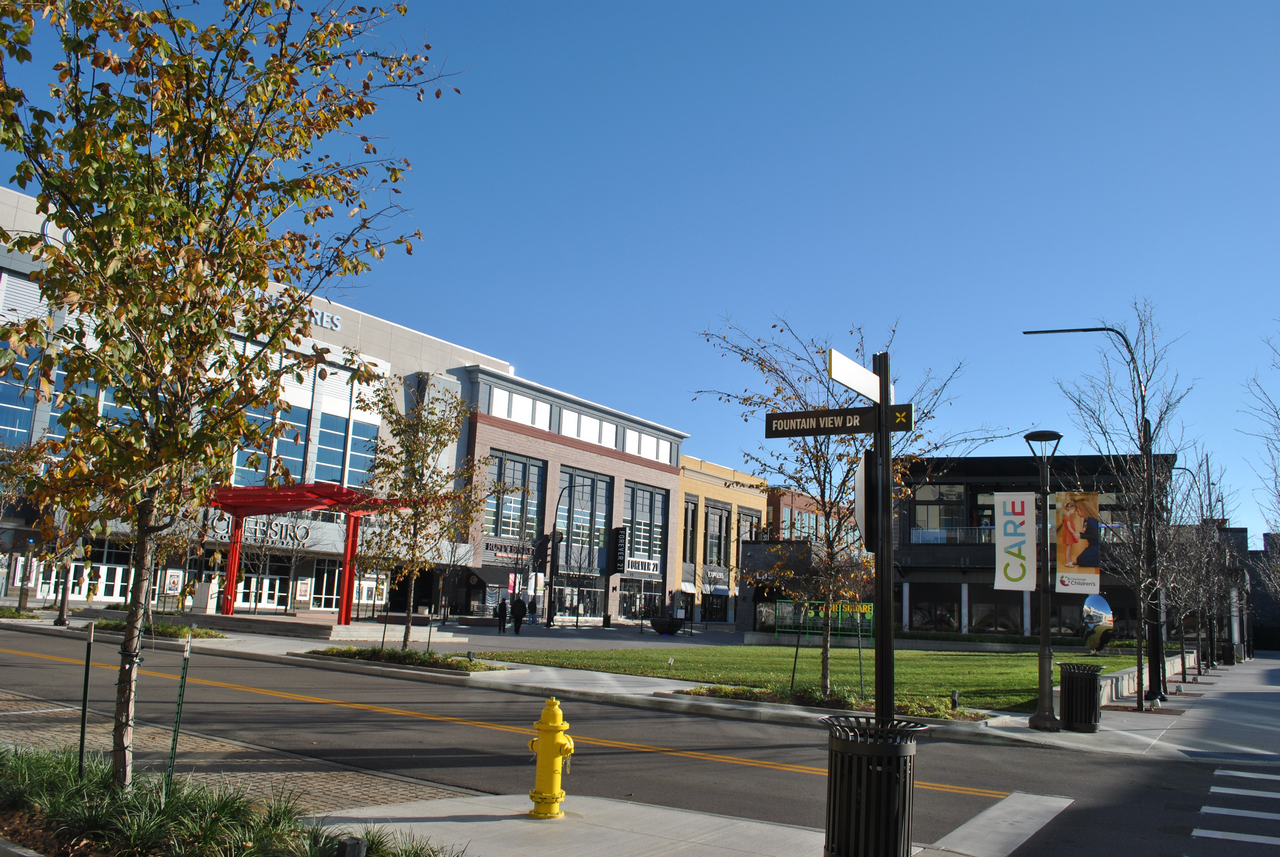 Urban street scene with buildings, trees, and a yellow fire hydrant under a clear blue sky.