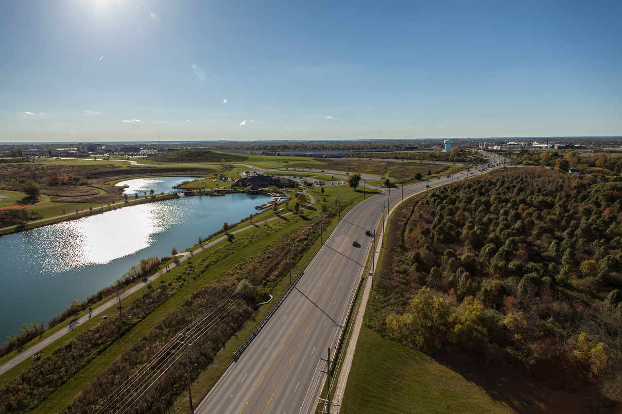 Aerial view of a road by a lake under a clear blue sky.