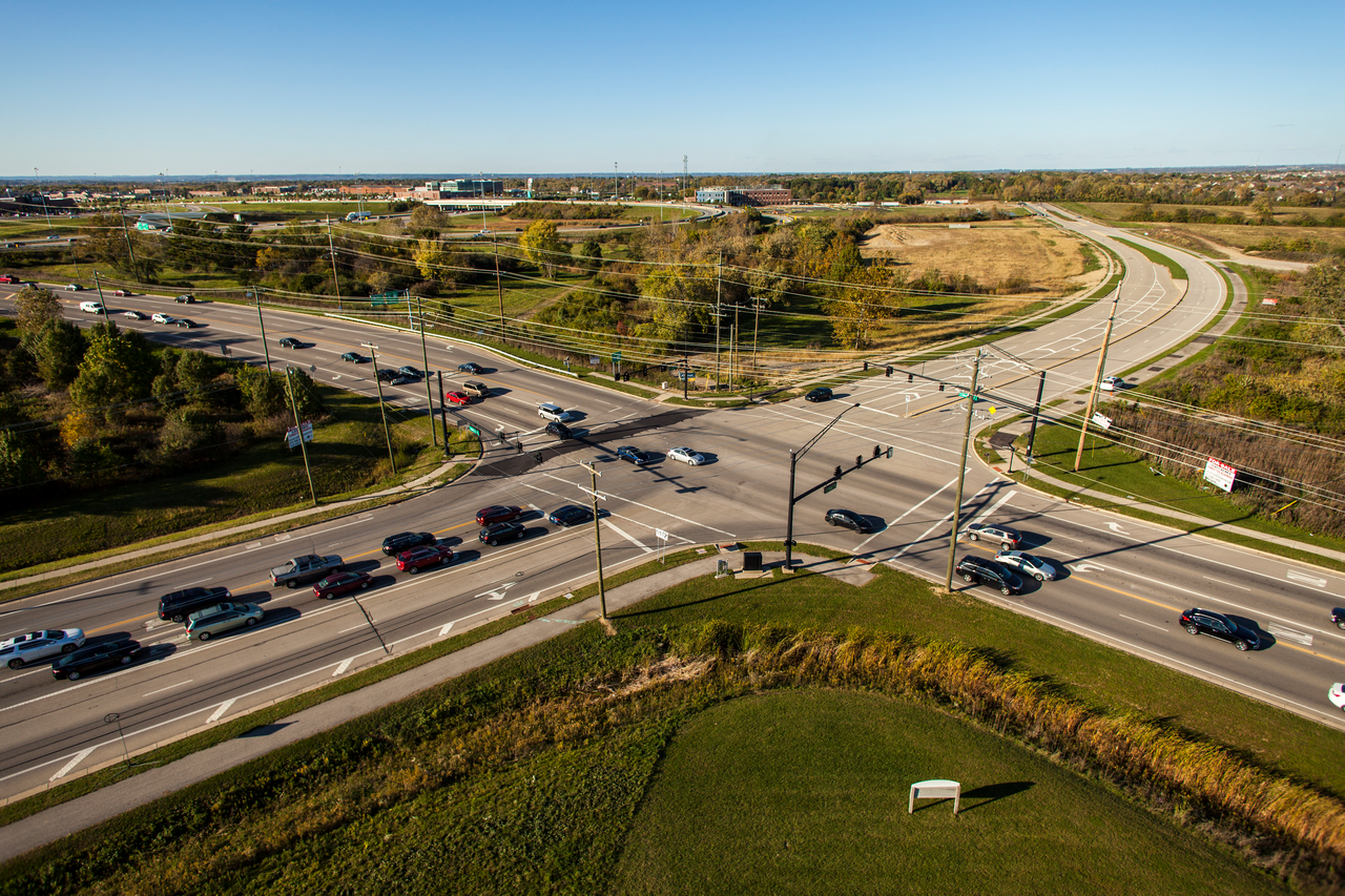 Aerial view of a busy crossroads, surrounded by greenery under a clear blue sky.