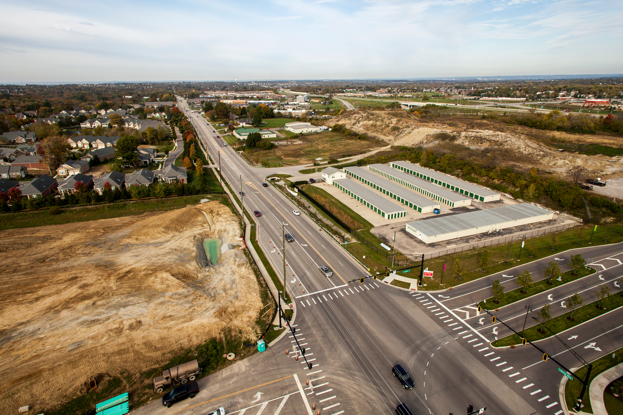 Aerial view of a wide intersection with sparse traffic and surrounding fields.