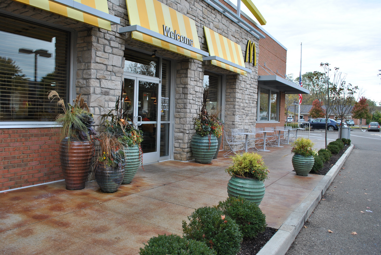 Storefront with stone facade, yellow-striped awnings, and plant pots on the sidewalk.