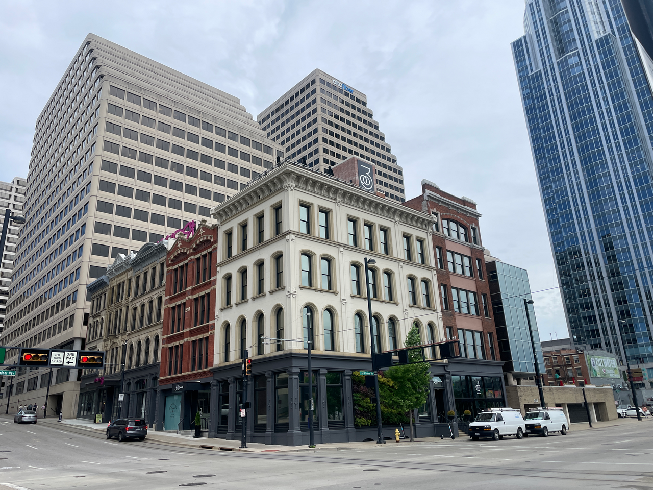 Older brick building surrounded by modern skyscrapers on a city street corner.