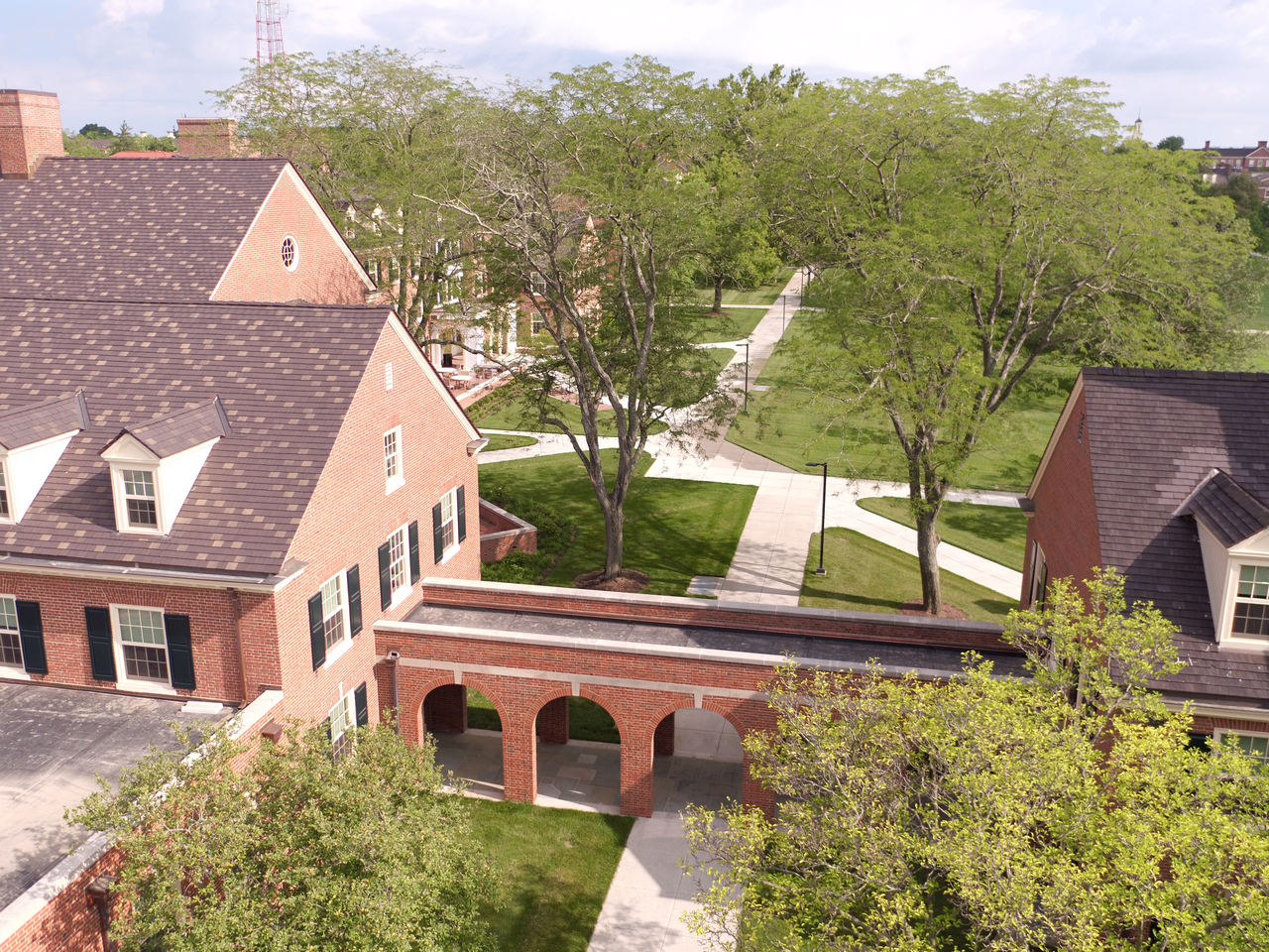 Brick building with archway, surrounded by trees and pathways on a sunny day.