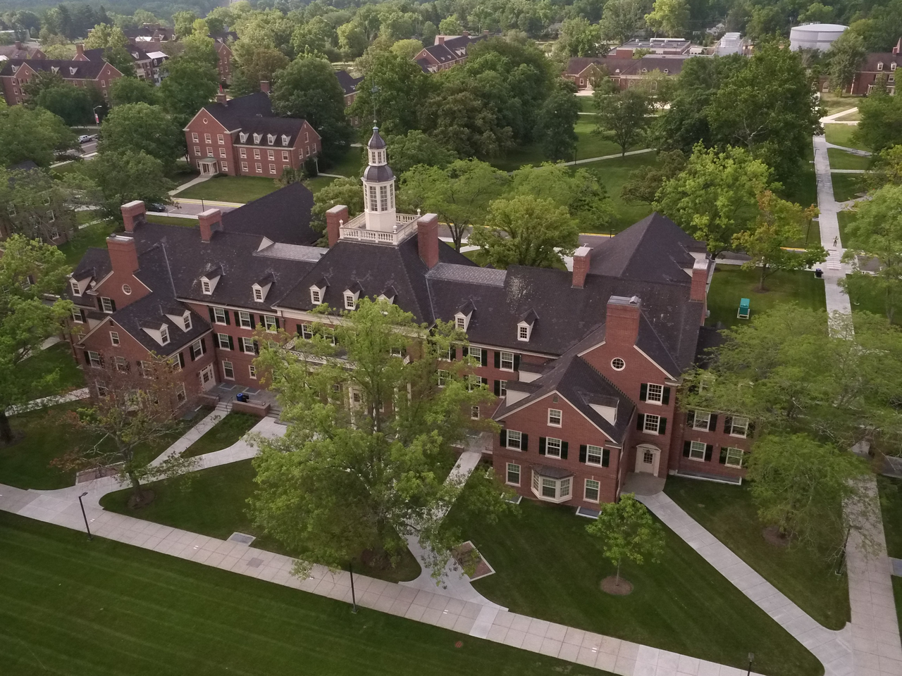 Red brick building with a central tower, surrounded by green trees.
