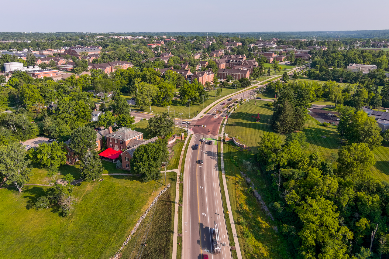 Aerial view of a road cutting through a green, leafy urban area.
