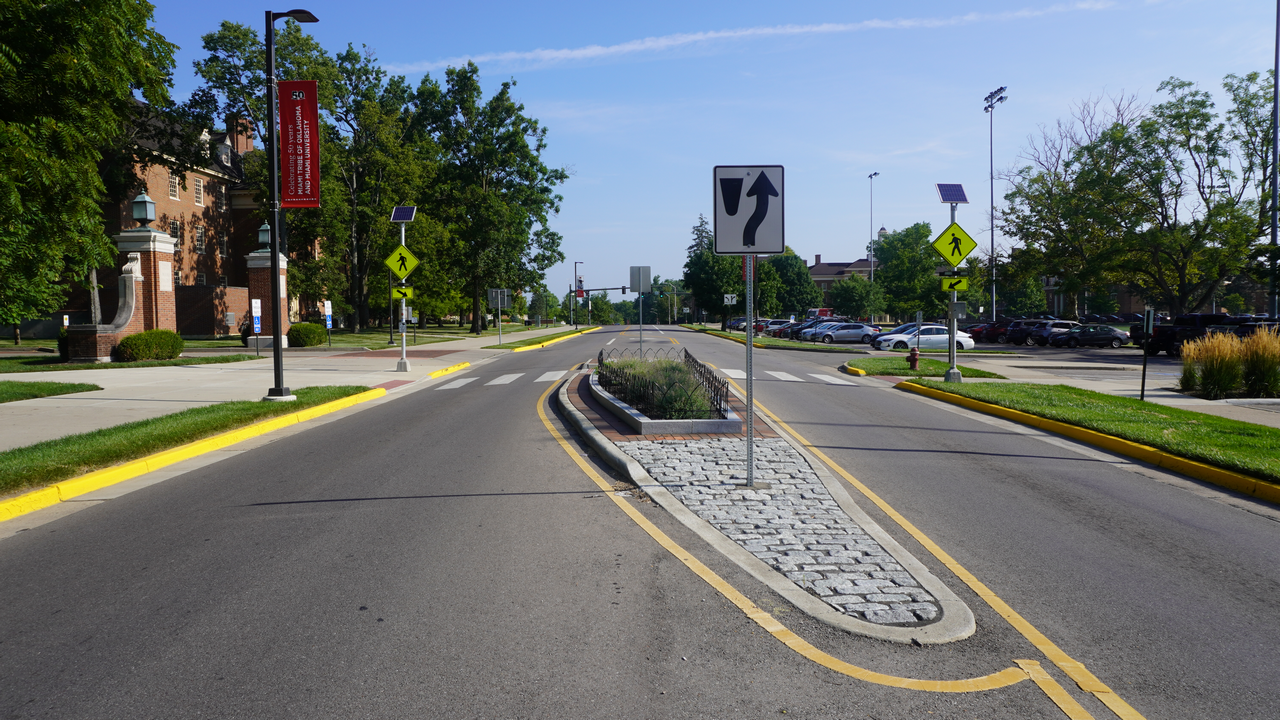 Divided road with a median and trees lining the sidewalks on a sunny day.