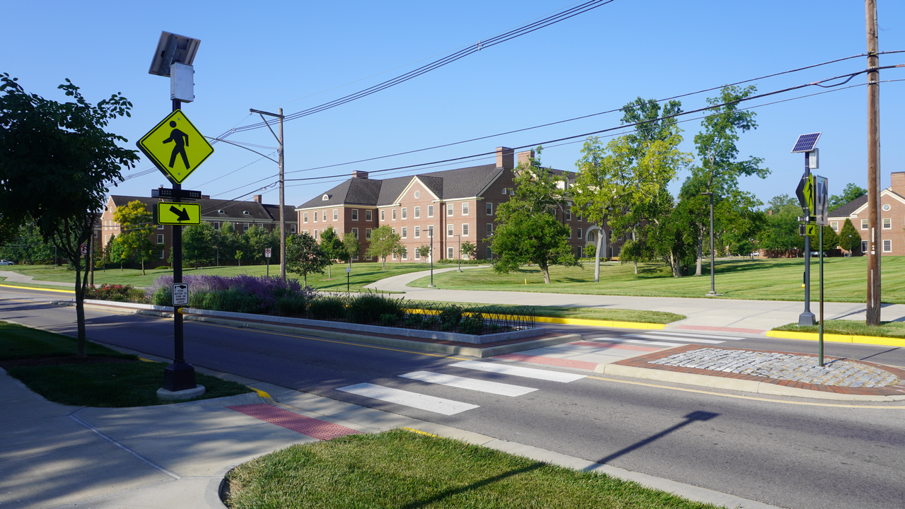 Crosswalk and brick buildings on a sunny day, with trees and green grass.