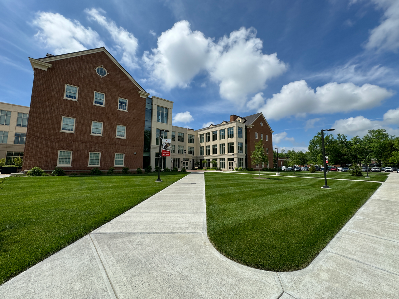 Brick and cream buildings on a grassy campus under a blue sky with clouds.