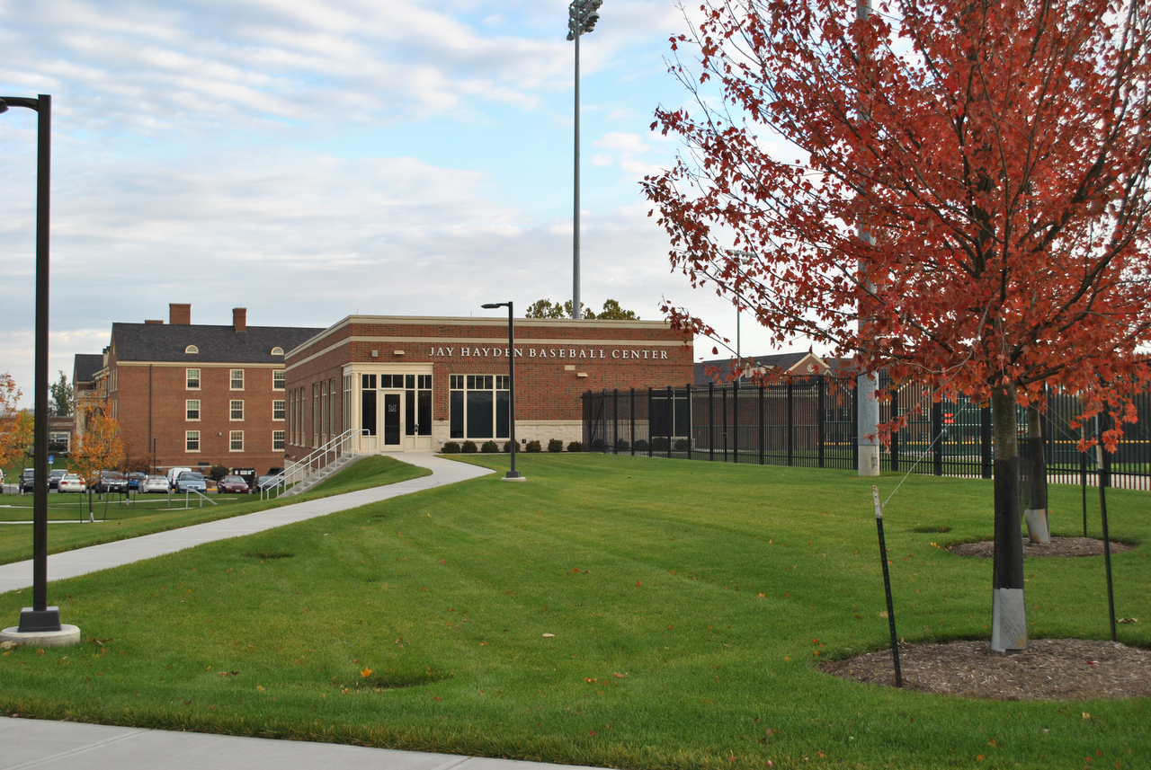 Campus building with lawn, red tree, and pathway under cloudy sky.