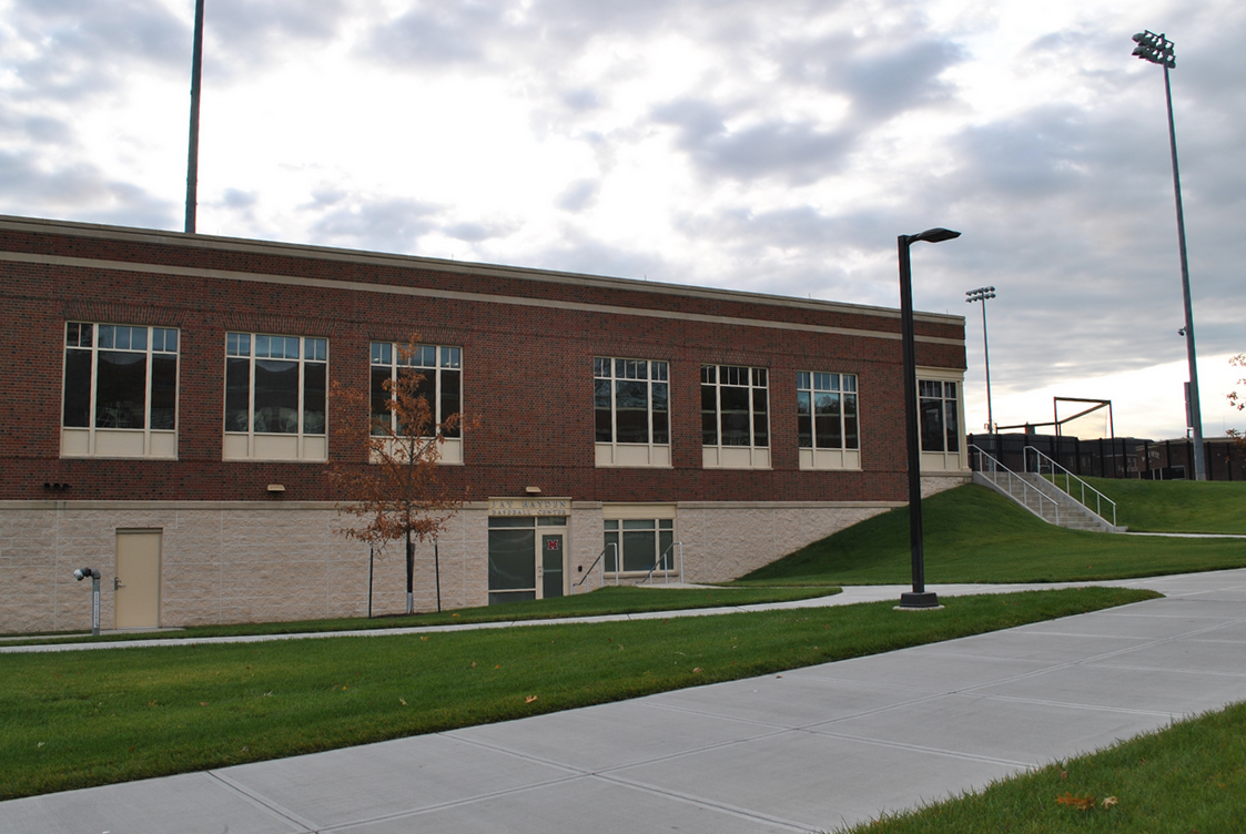 Brick building with large windows, overcast sky above, surrounded by green grass and pathways.