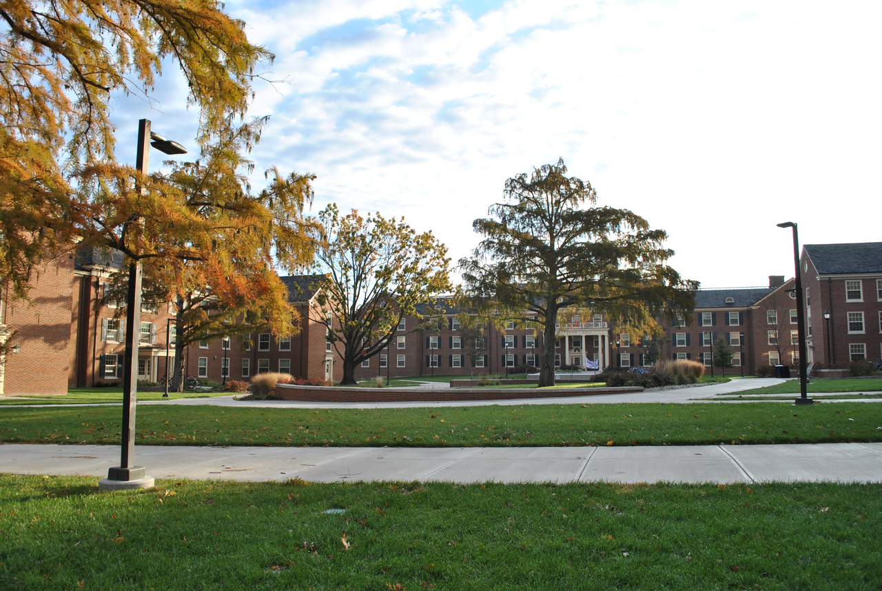 Campus courtyard with brick buildings, trees, and a cloudy sky.