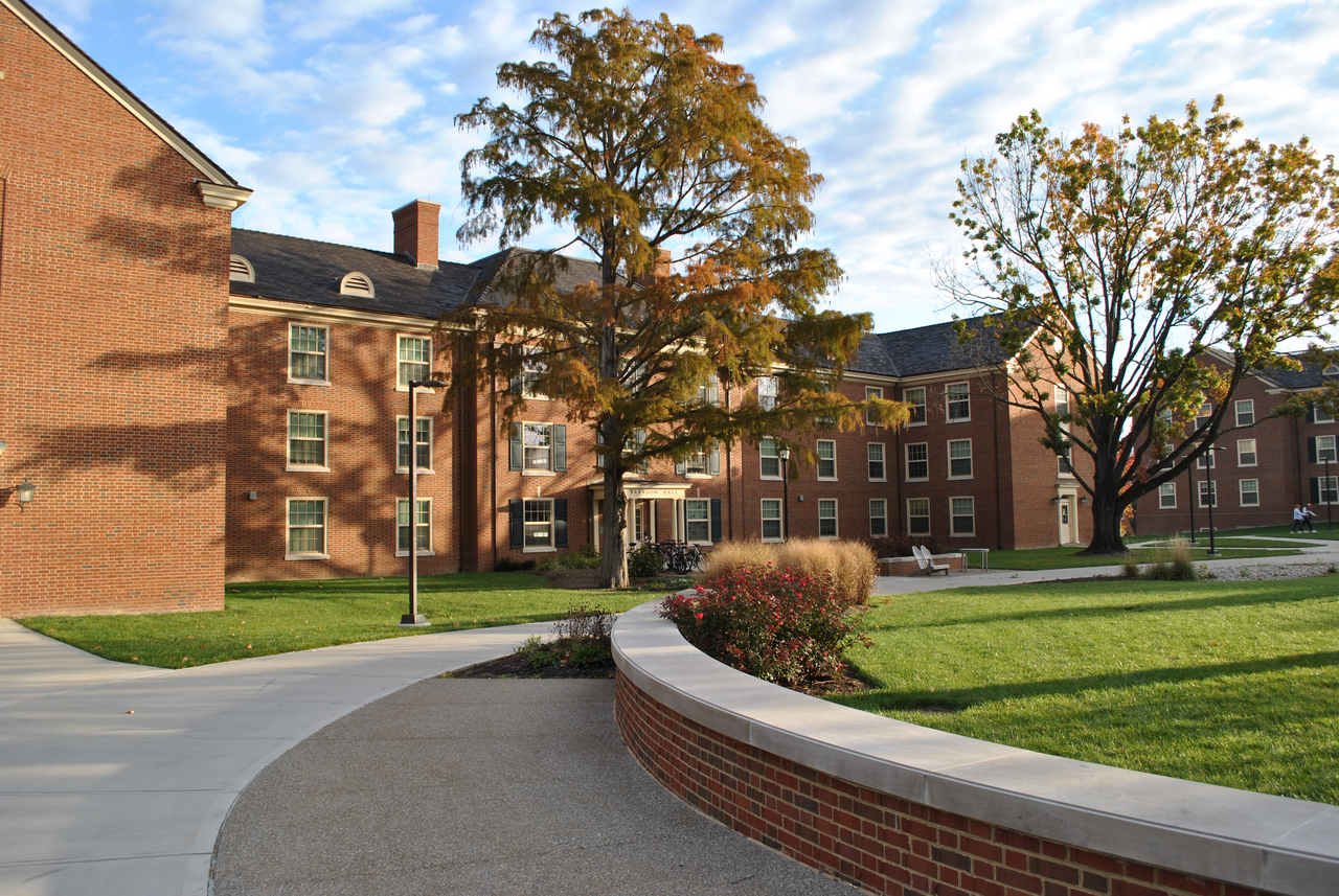 Campus courtyard with red-brick buildings, trees, and a curved pathway.