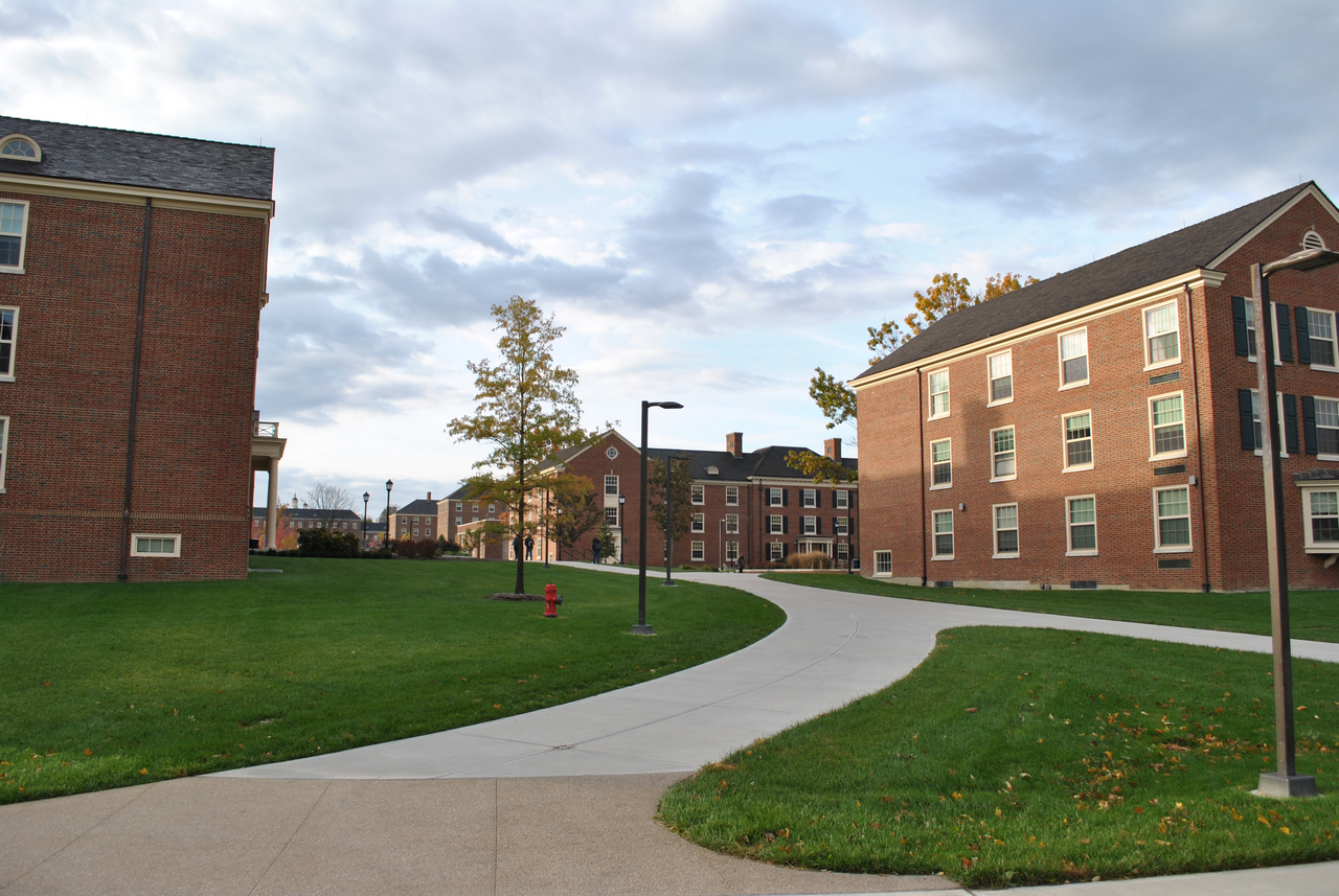Campus pathway between red brick buildings under a cloudy sky.