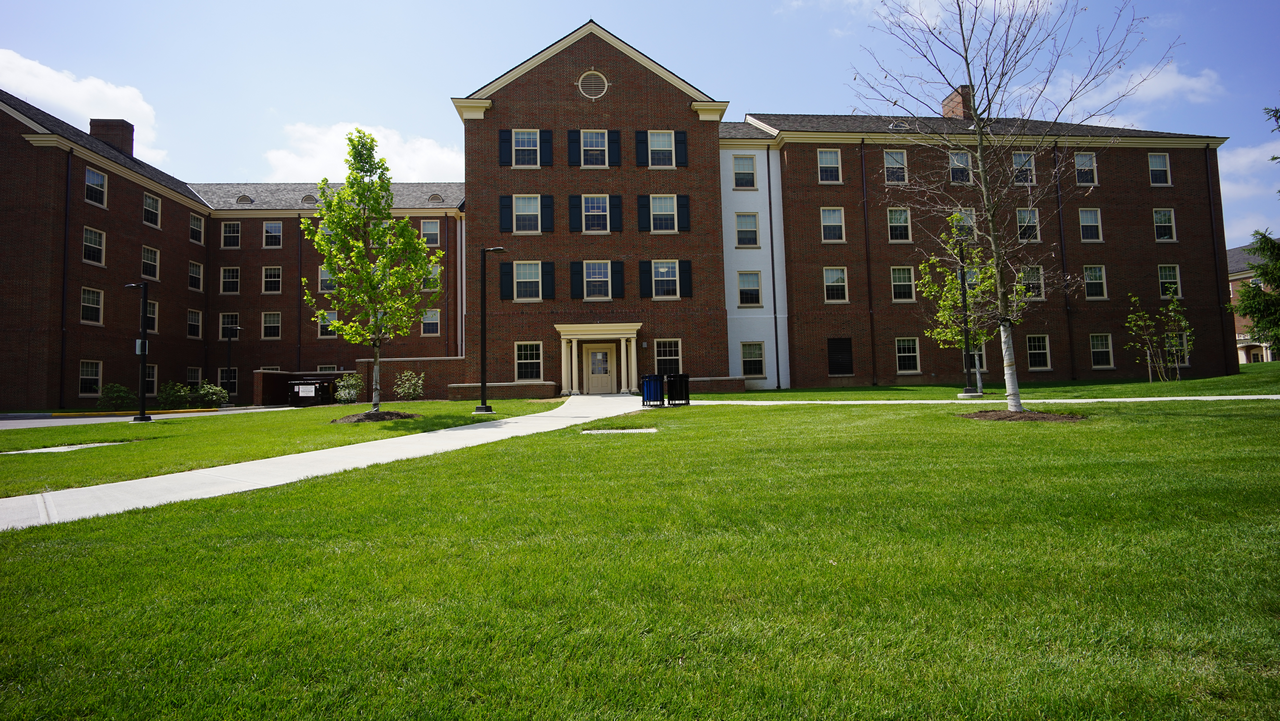 College campus with a large brick building, green lawn, and clear sky.