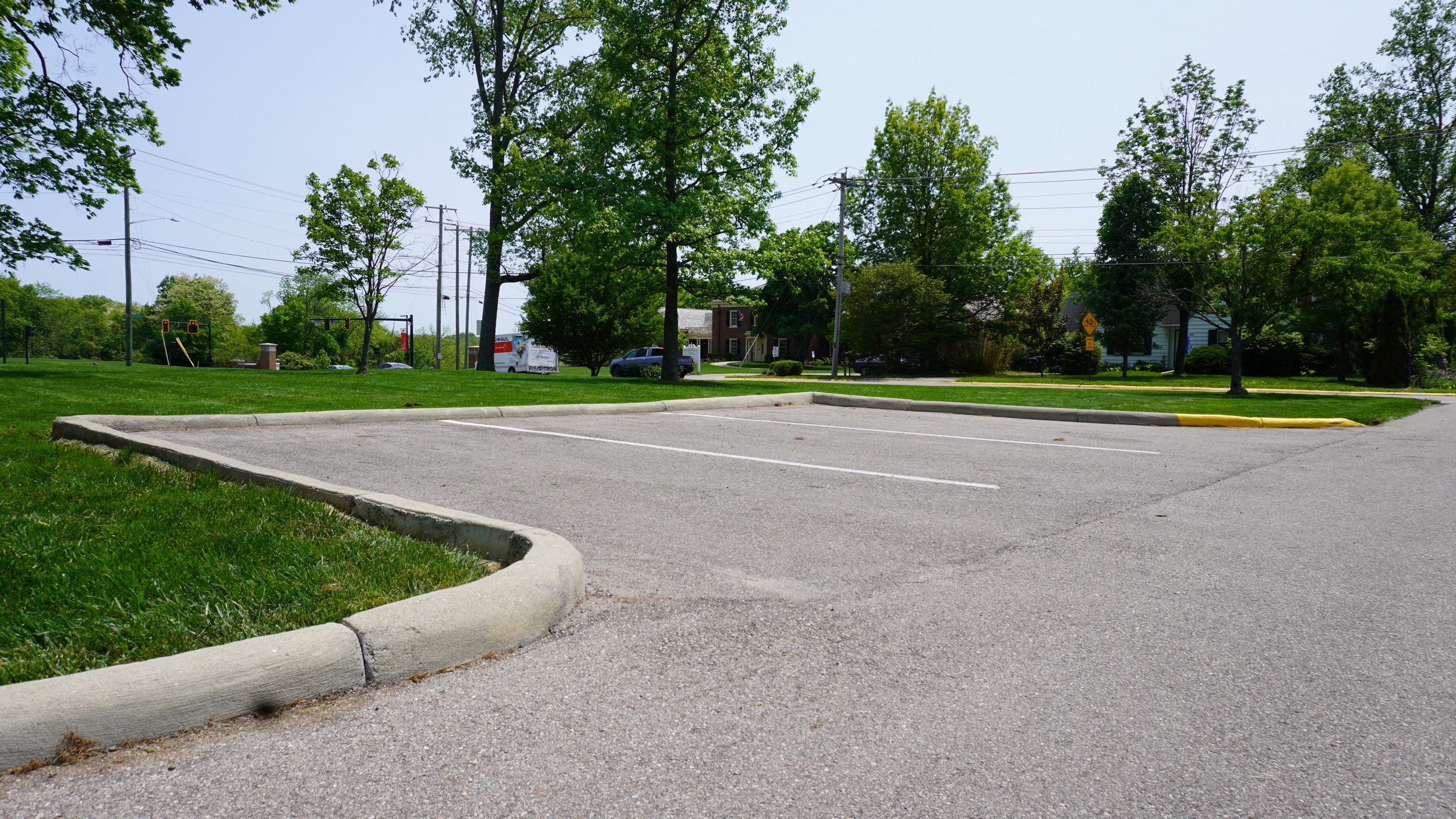 Empty parking lot bordered by grass and trees on a clear day.