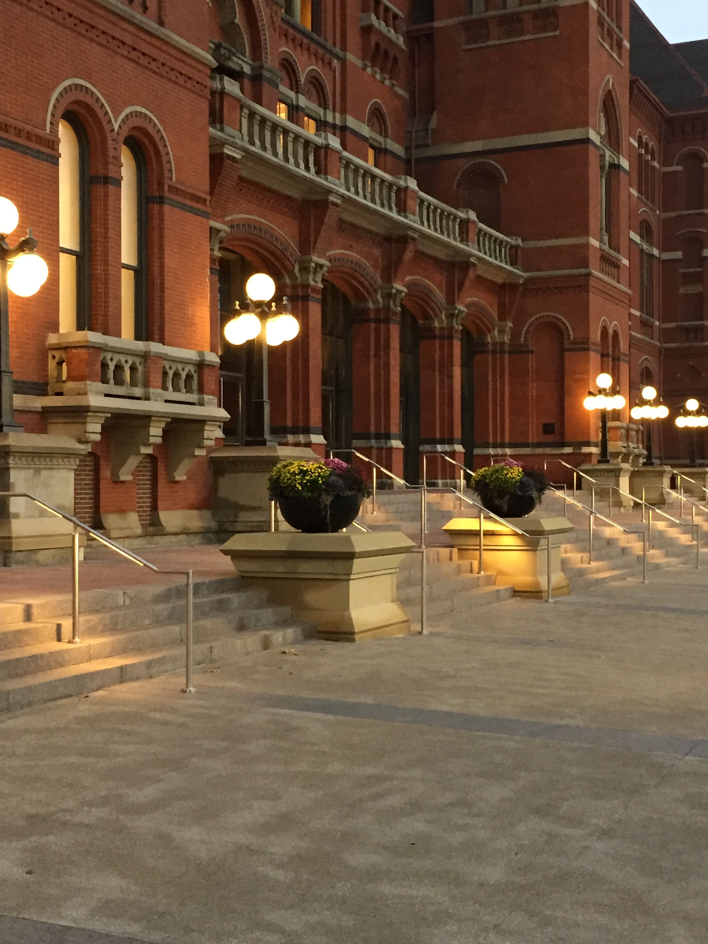 Illuminated brick building with stairs and potted plants at dusk.