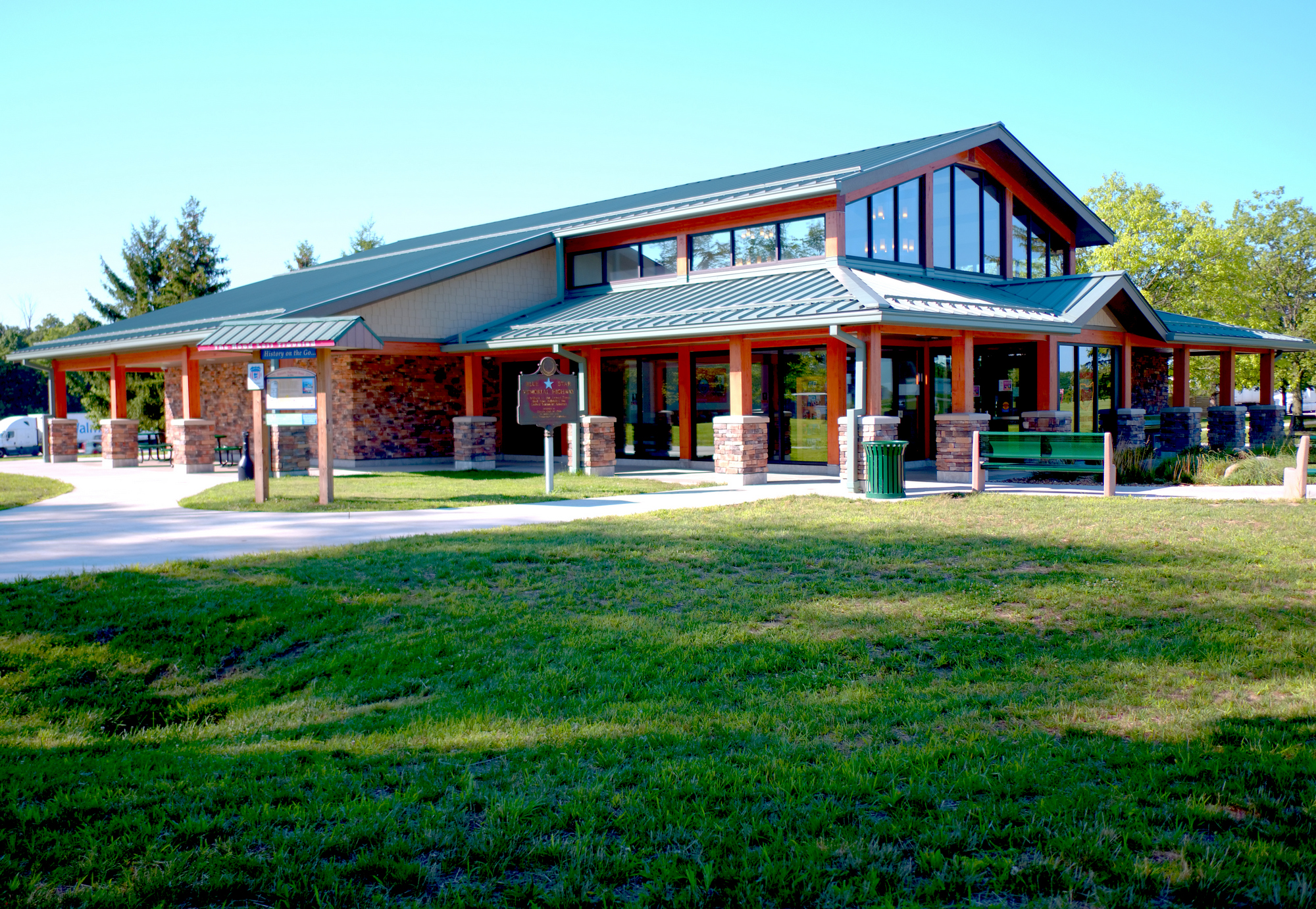 Modern building with green roof, surrounded by trees and grass on a sunny day.