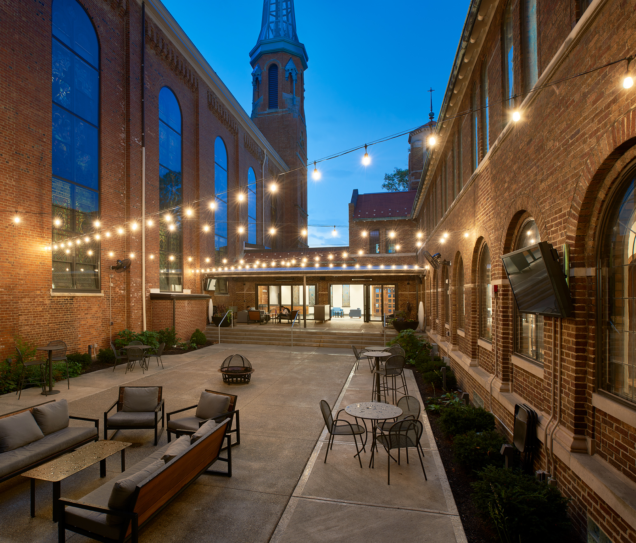 Cozy courtyard with string lights, outdoor seating, and brick buildings at dusk.
