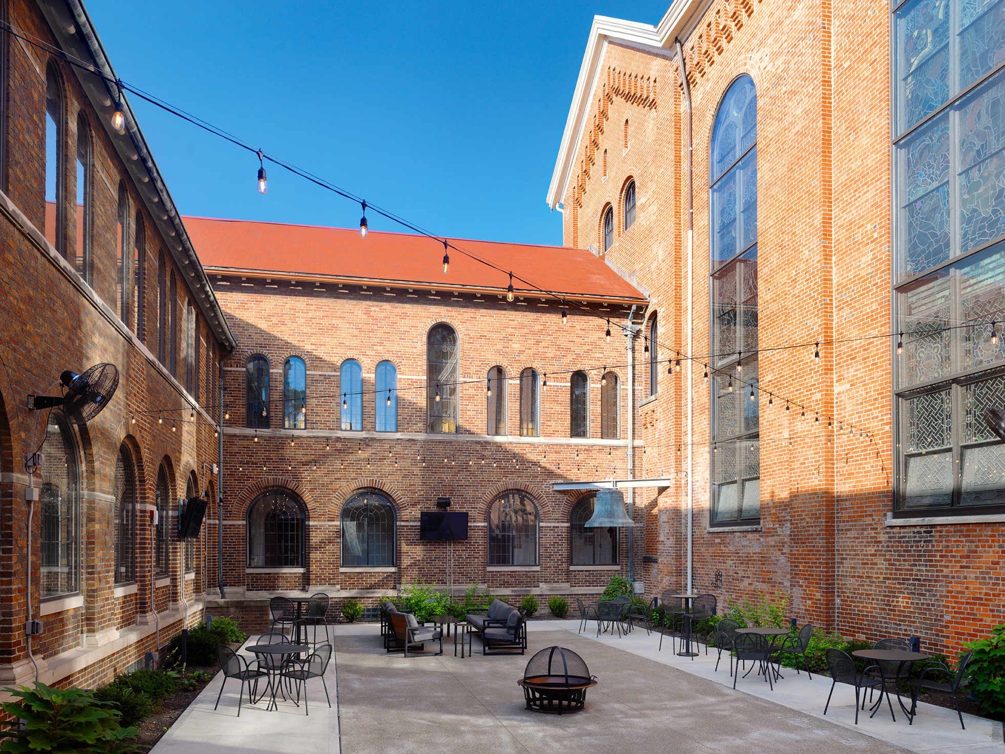 Brick courtyard with string lights and outdoor seating under a clear blue sky.