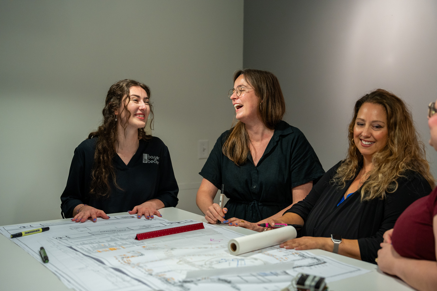 Bayer Becker Is Down To Earth Women smiling and discussing over architectural plans at a table.