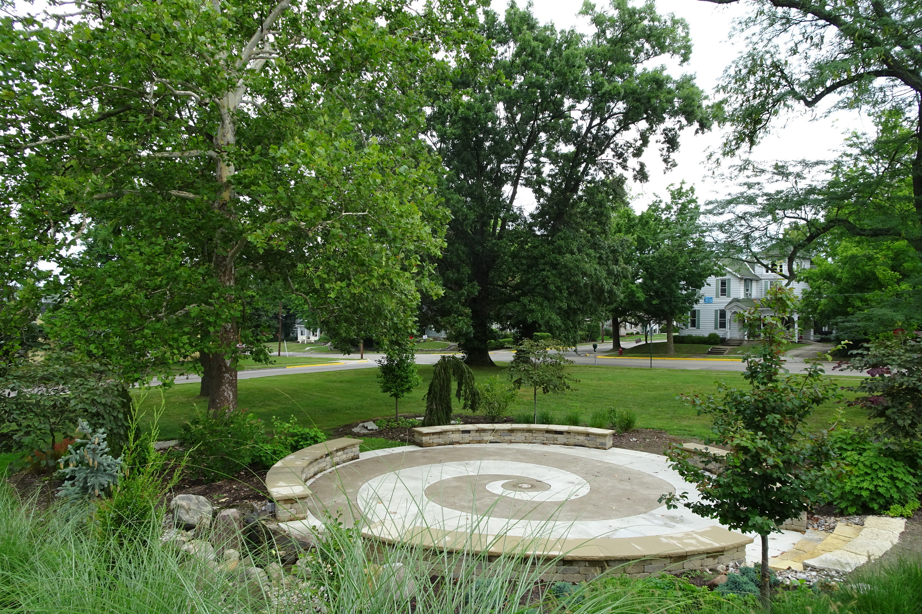 Circular stone patio with spiral design, surrounded by trees and grass.