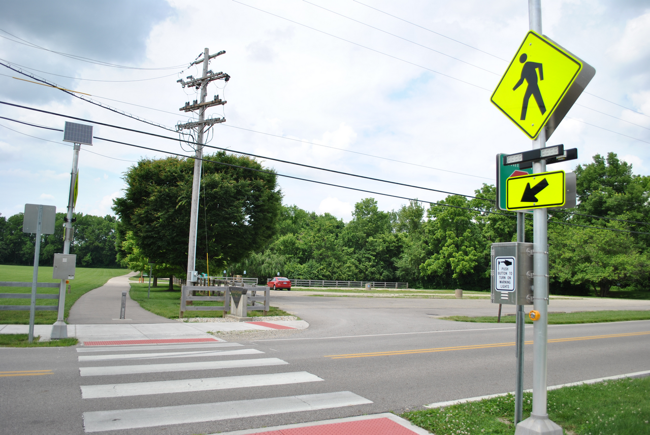 Crosswalk near a road with pedestrian signs and lush greenery.