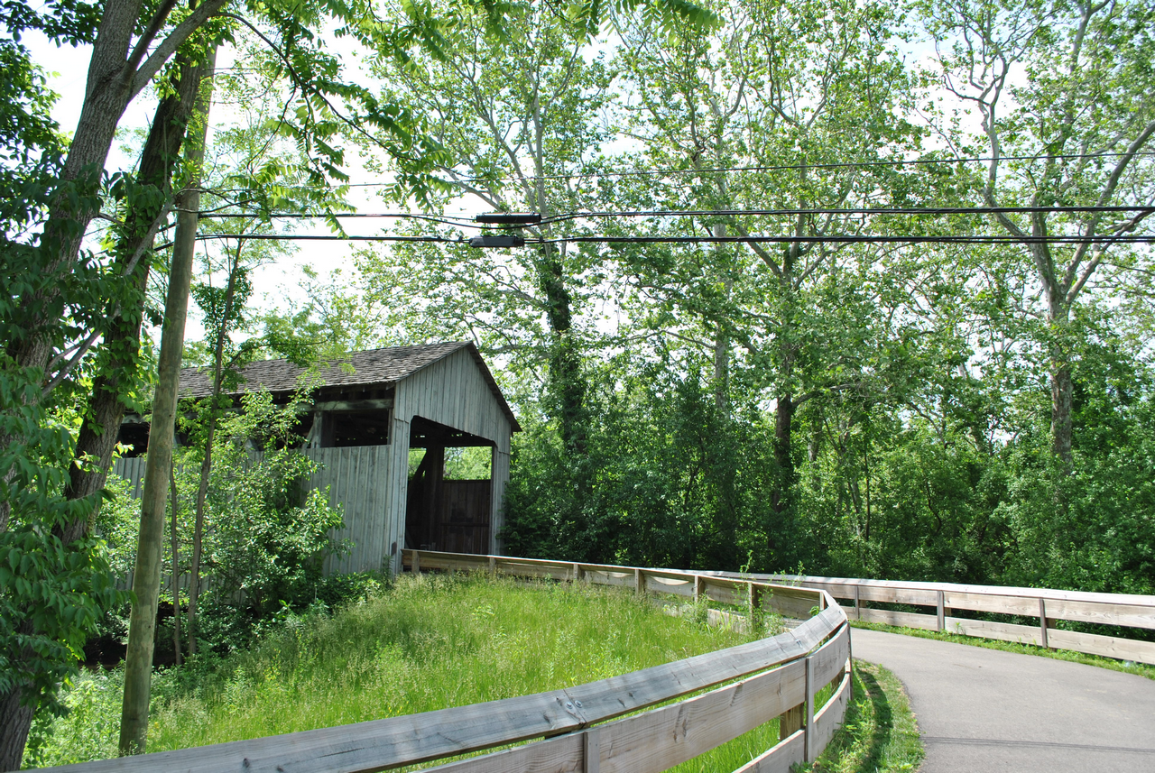 Covered bridge by winding path surrounded by green trees.