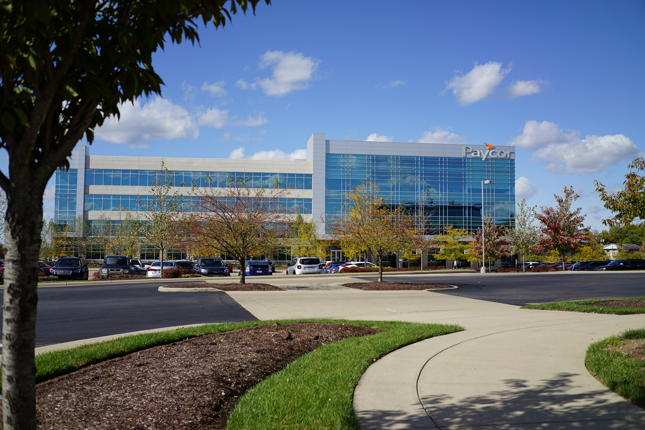 Corporate building with glass facade under blue sky, surrounded by autumn trees.