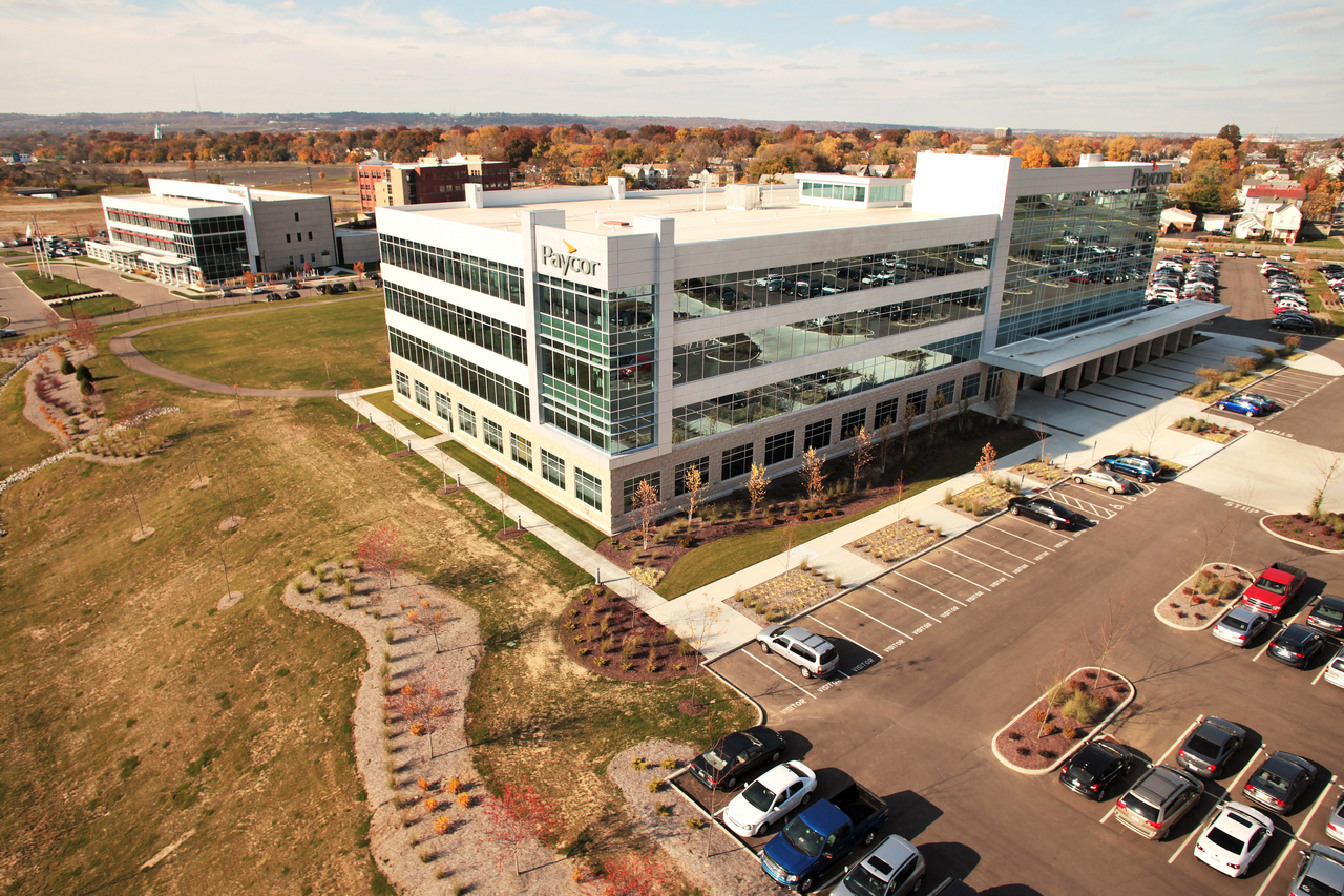 Four-story office building with large windows, parking lot, and surrounding green space.