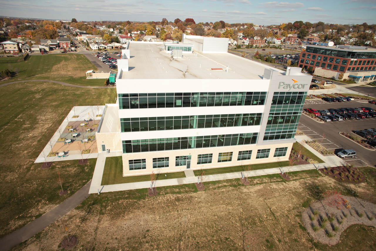 Four-story office building with a parking lot, surrounded by grassy fields.