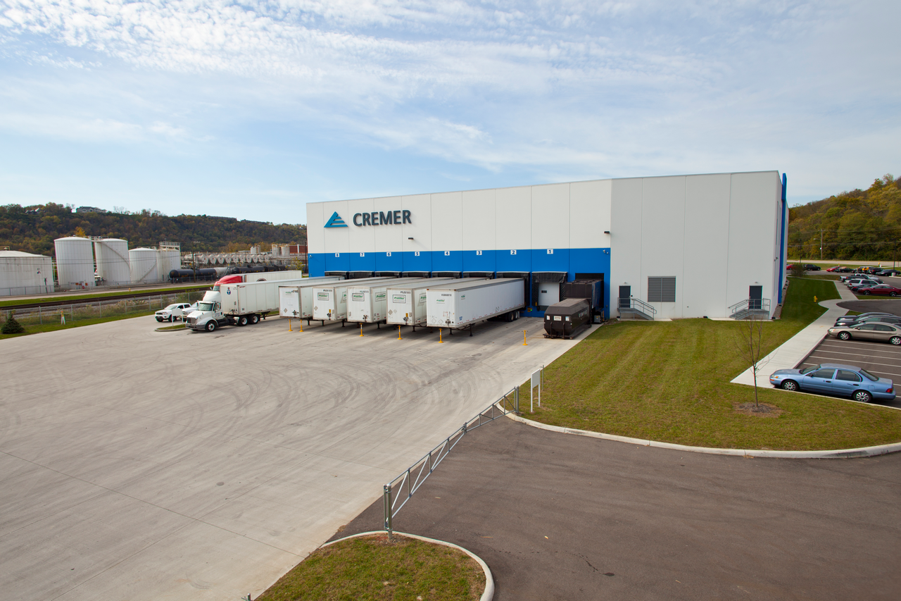 Large warehouse with trucks parked, grassy area to the side.