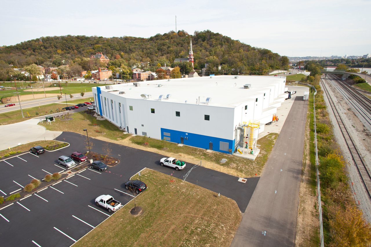 Large white building with blue accents in a grassy area, parking lot in foreground.