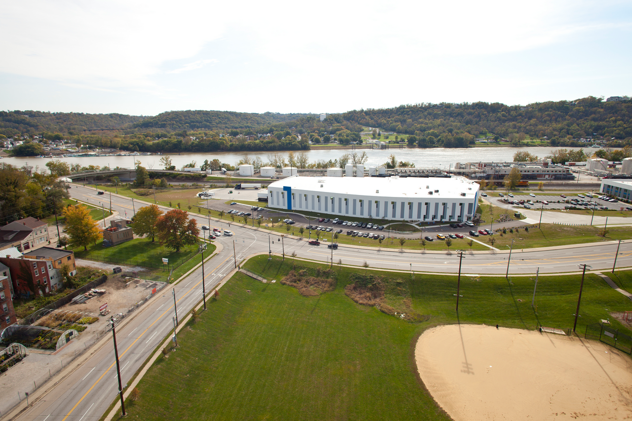 View of a curved road with a large white building beside it, near a river and hills.