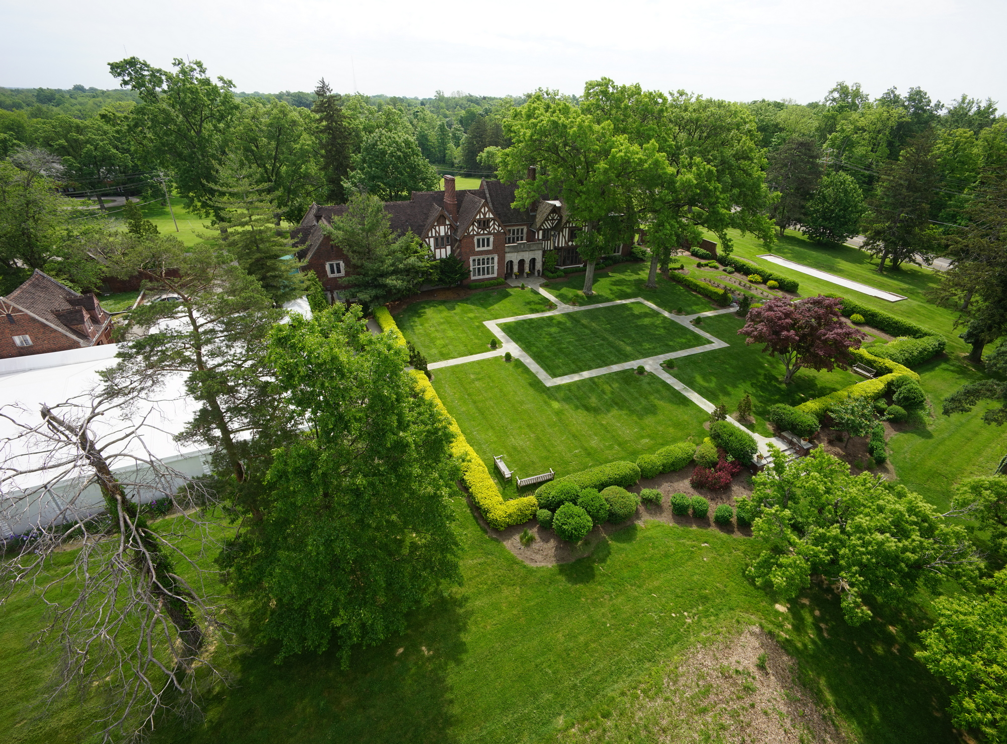 Aerial view of a large garden with manicured lawns and a brick house surrounded by trees.