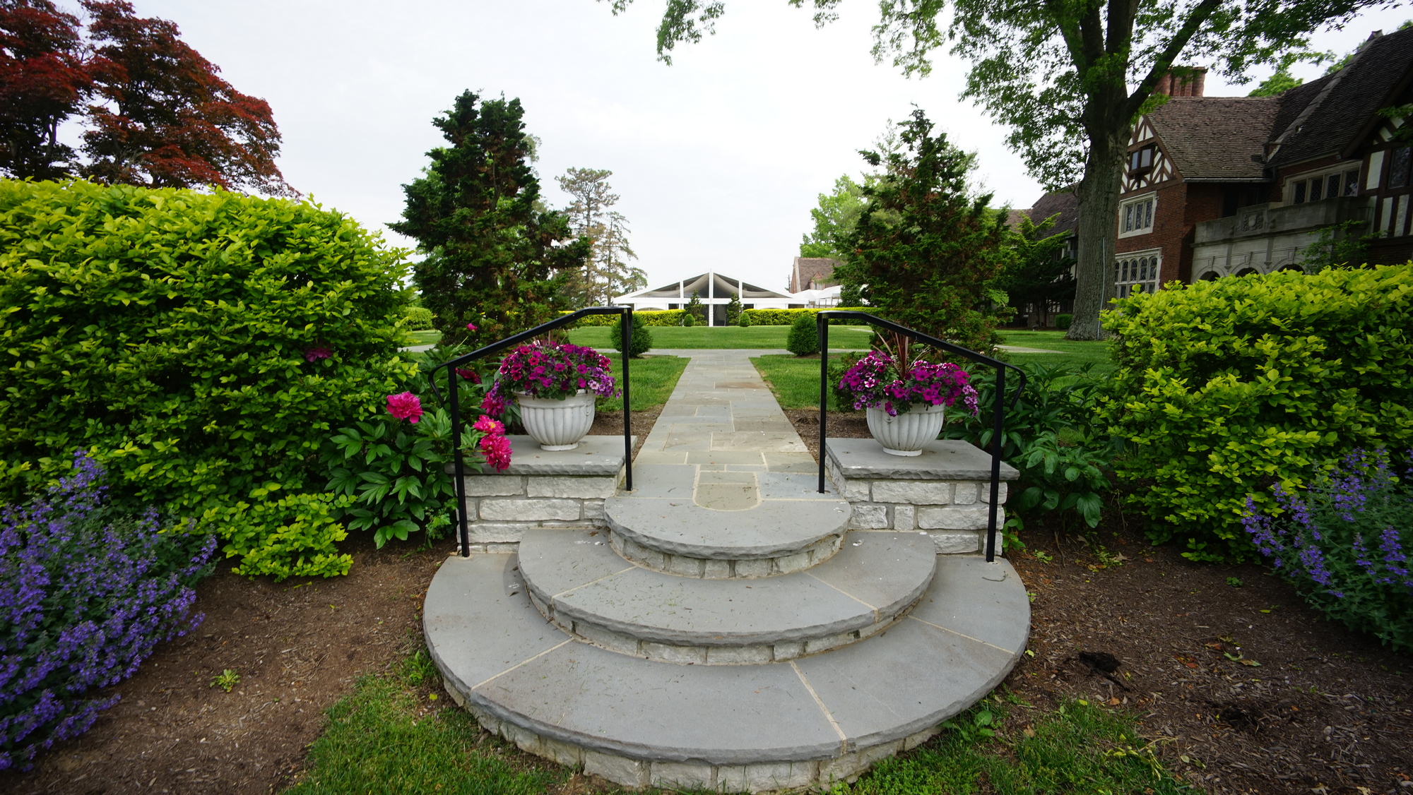 Stone steps lead to garden path, lined with bushes and flowers.