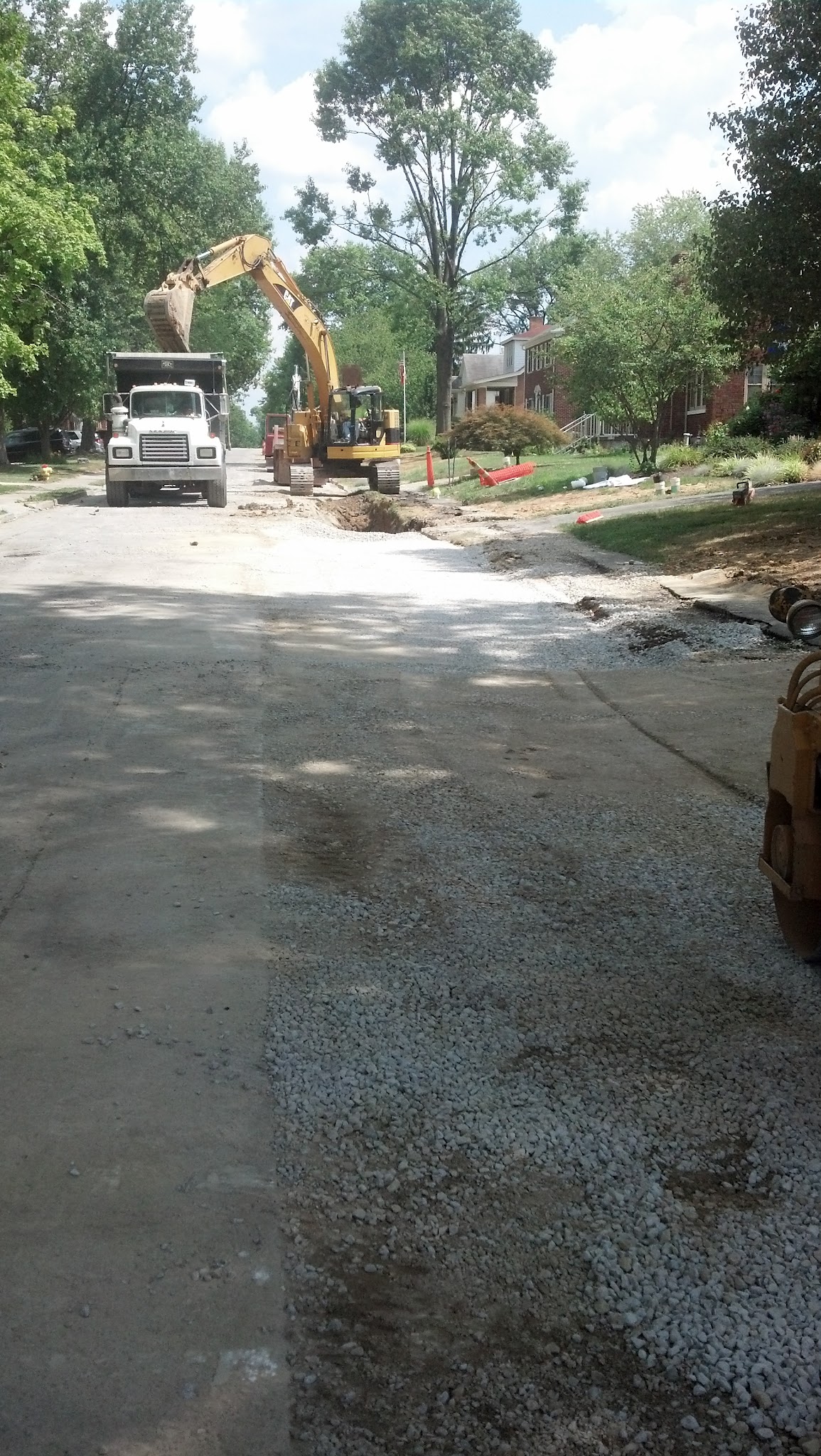 Construction site on a residential street with trees and machinery.