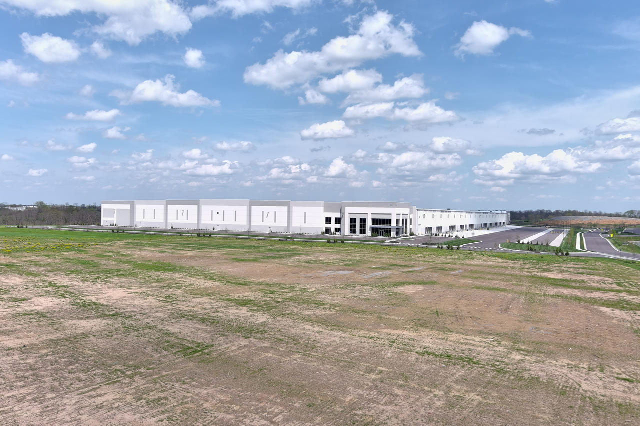 Large white warehouse in an open field under a partly cloudy sky.