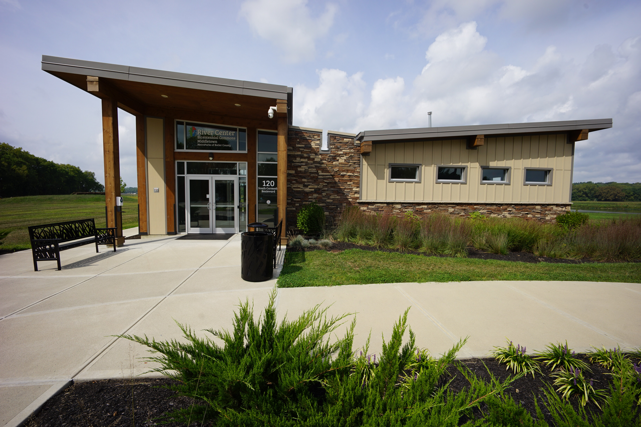 Modern building with stone and beige siding, surrounded by greenery under a cloudy sky.