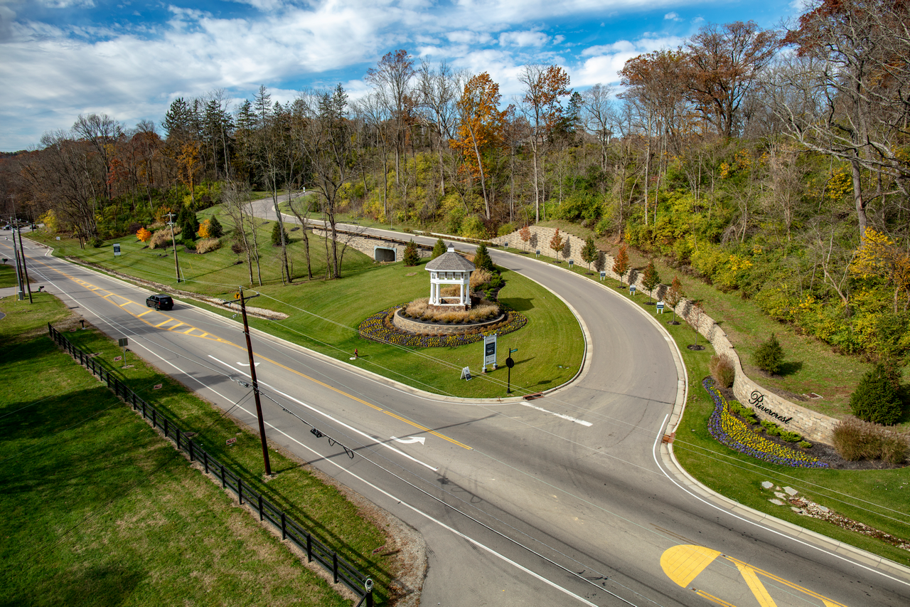 Curving road with a gazebo and landscaped hills under a partly cloudy sky.