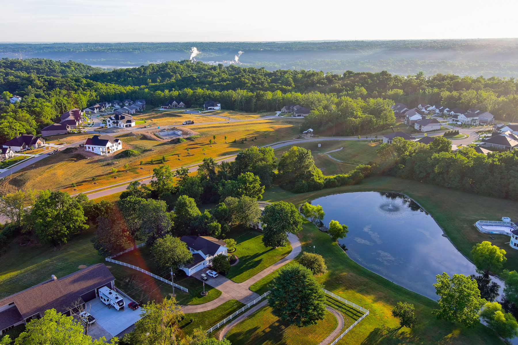 Aerial view of a suburban neighborhood with trees, houses, and a small pond.