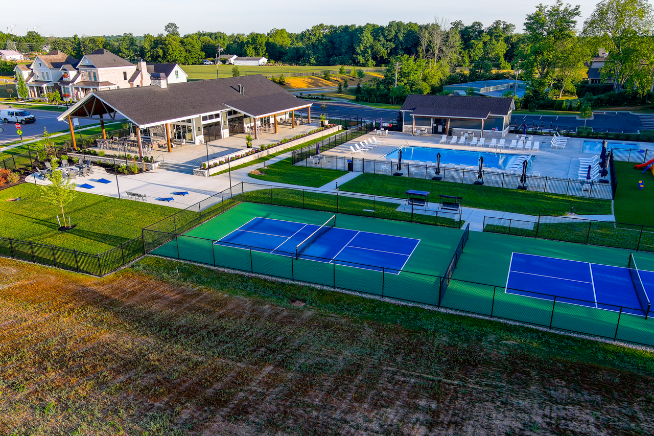 Clubhouse with tennis courts and a swimming pool in a lush green setting.