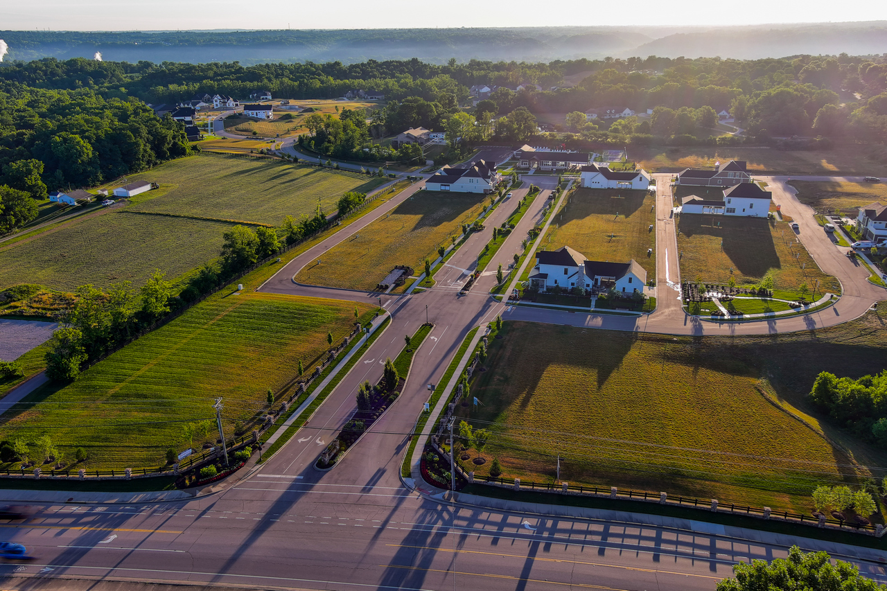 Aerial view of suburban housing with green fields and trees at sunset.