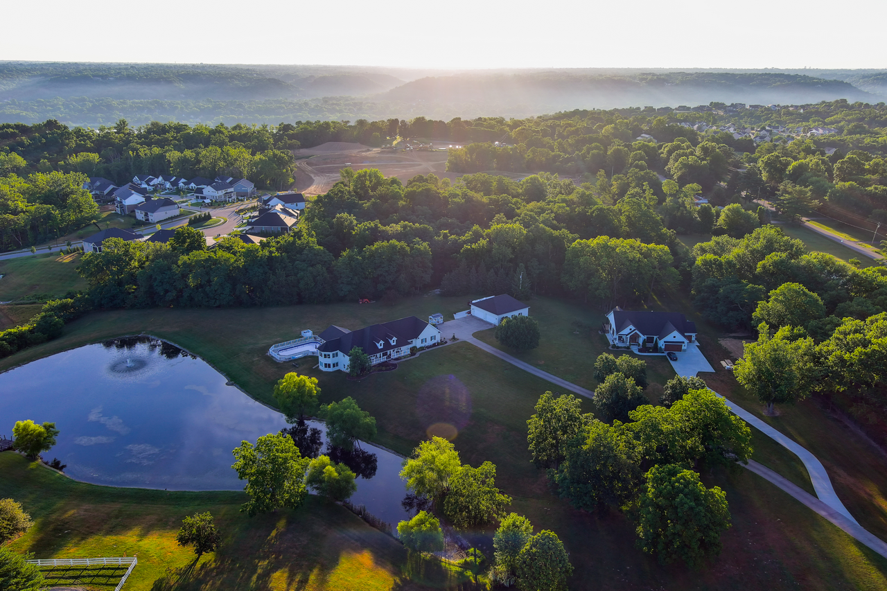 Aerial view of houses, trees, and a pond at sunrise.
