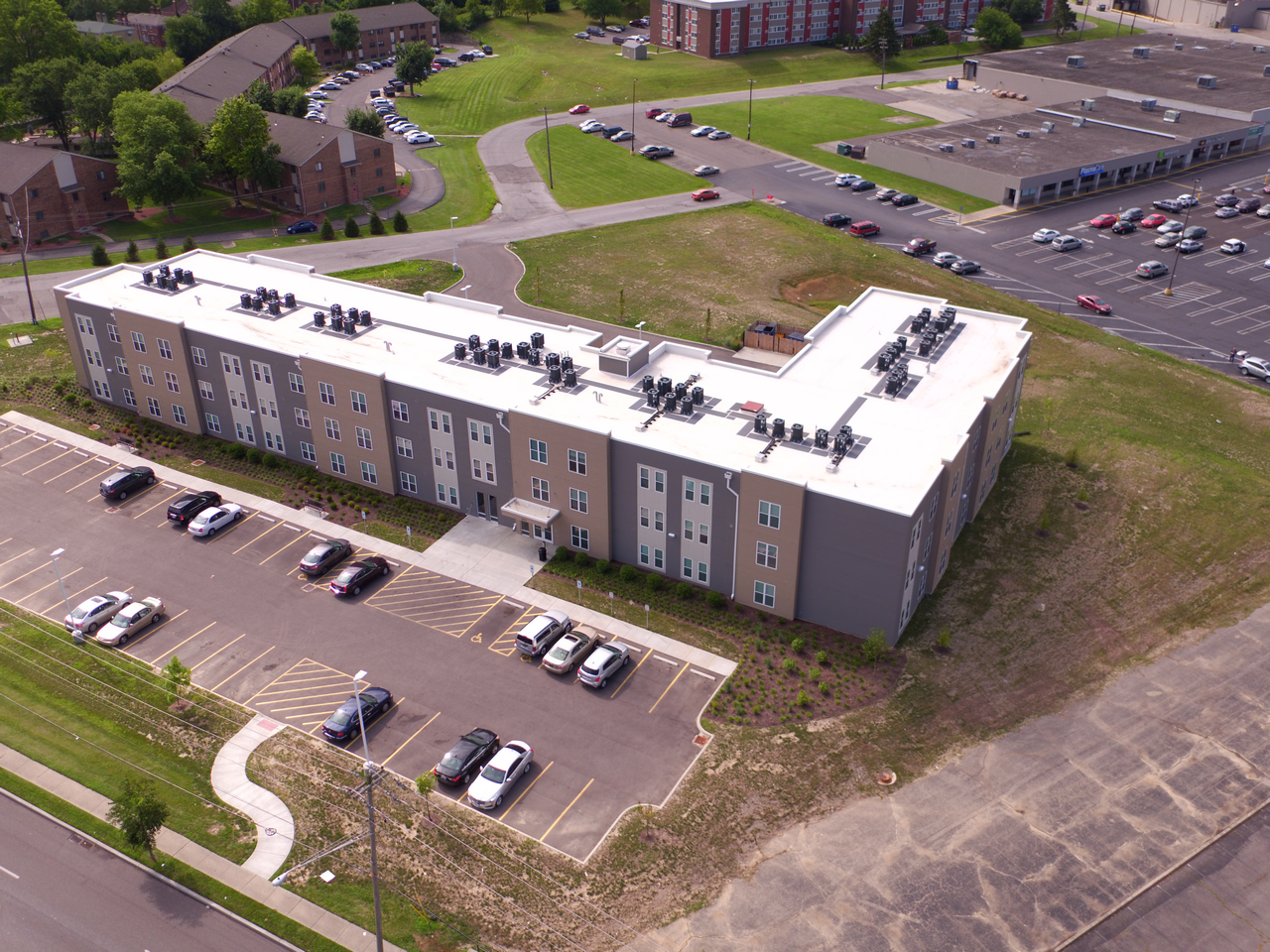 Aerial view of a large, L-shaped building with parking spaces and a green lawn.