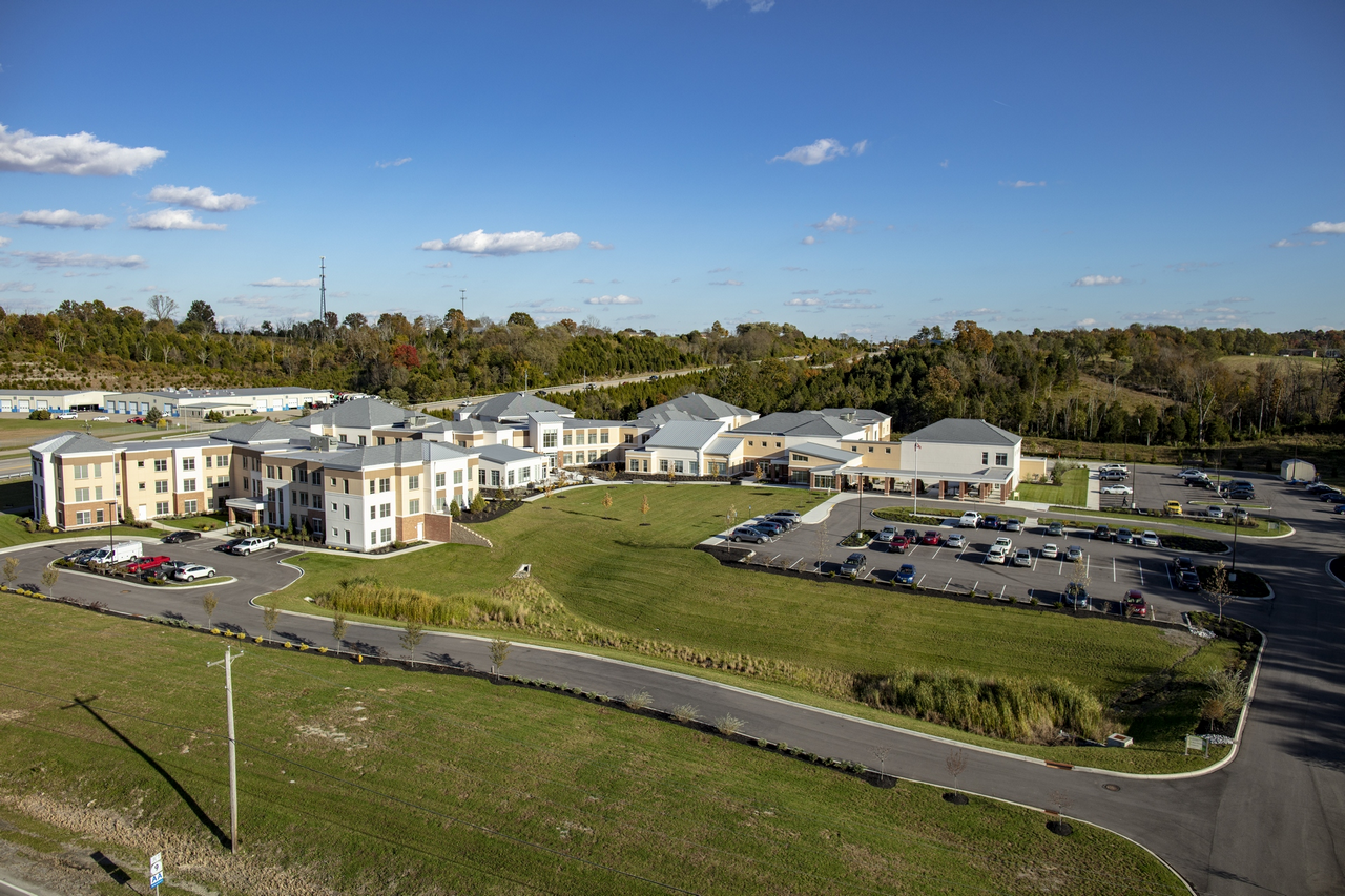 Aerial view of a large building complex with parking lots, surrounded by green fields under a blue sky.