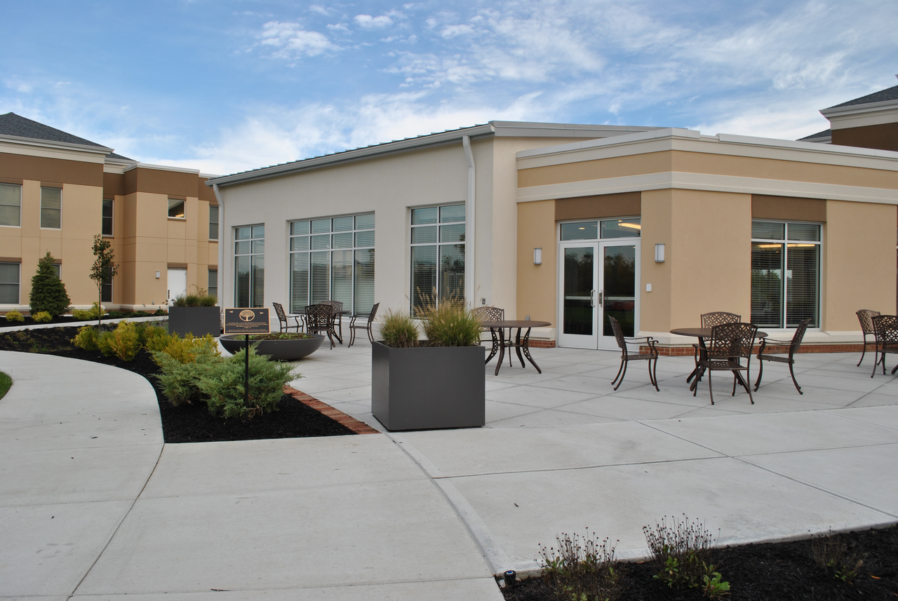 Modern patio with tables, chairs, and planters outside beige building under blue sky.