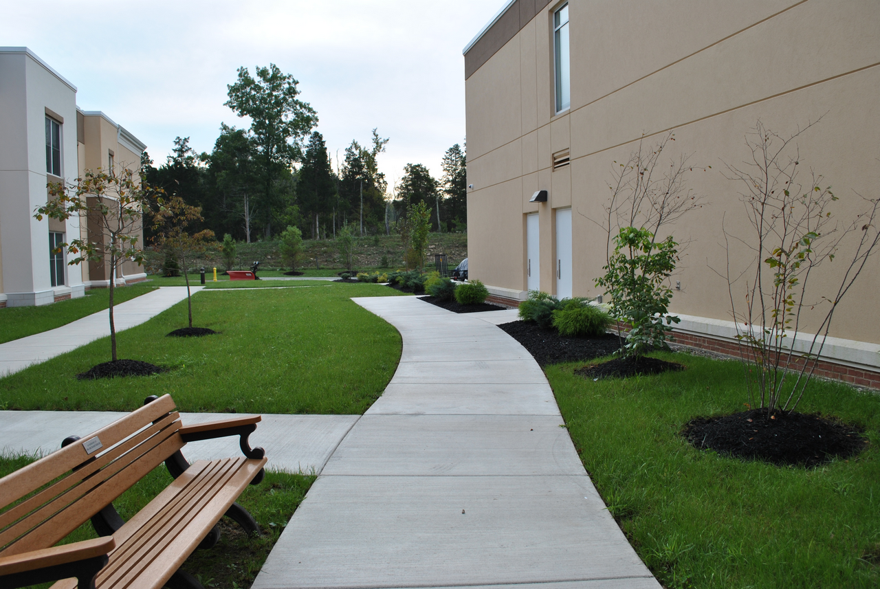 Pathway between buildings with green lawns and benches.