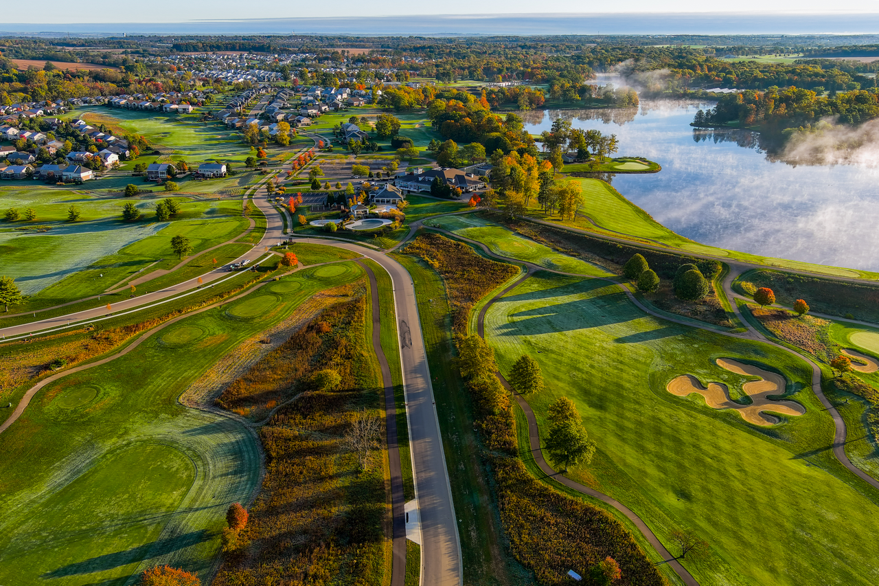 Aerial view of a golf course with a scenic lake and autumn-colored trees.