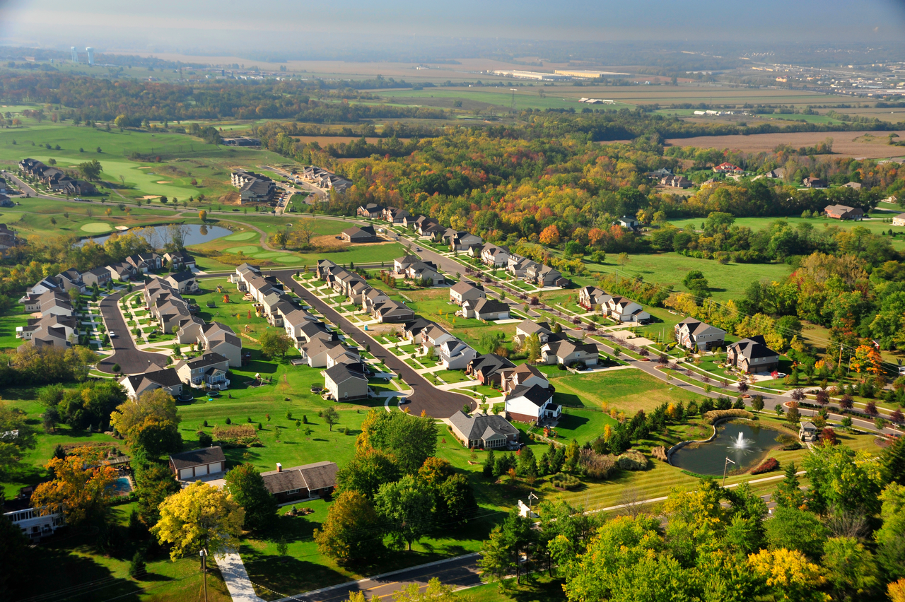Aerial view of suburban neighborhood surrounded by lush greenery and open fields.