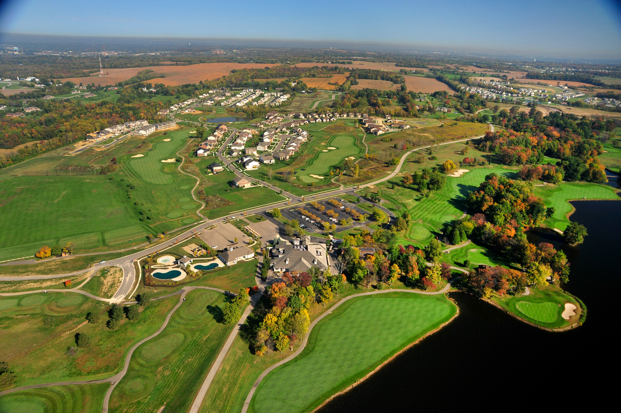 Aerial view of a golf course with lush greens and a clubhouse near a lake.